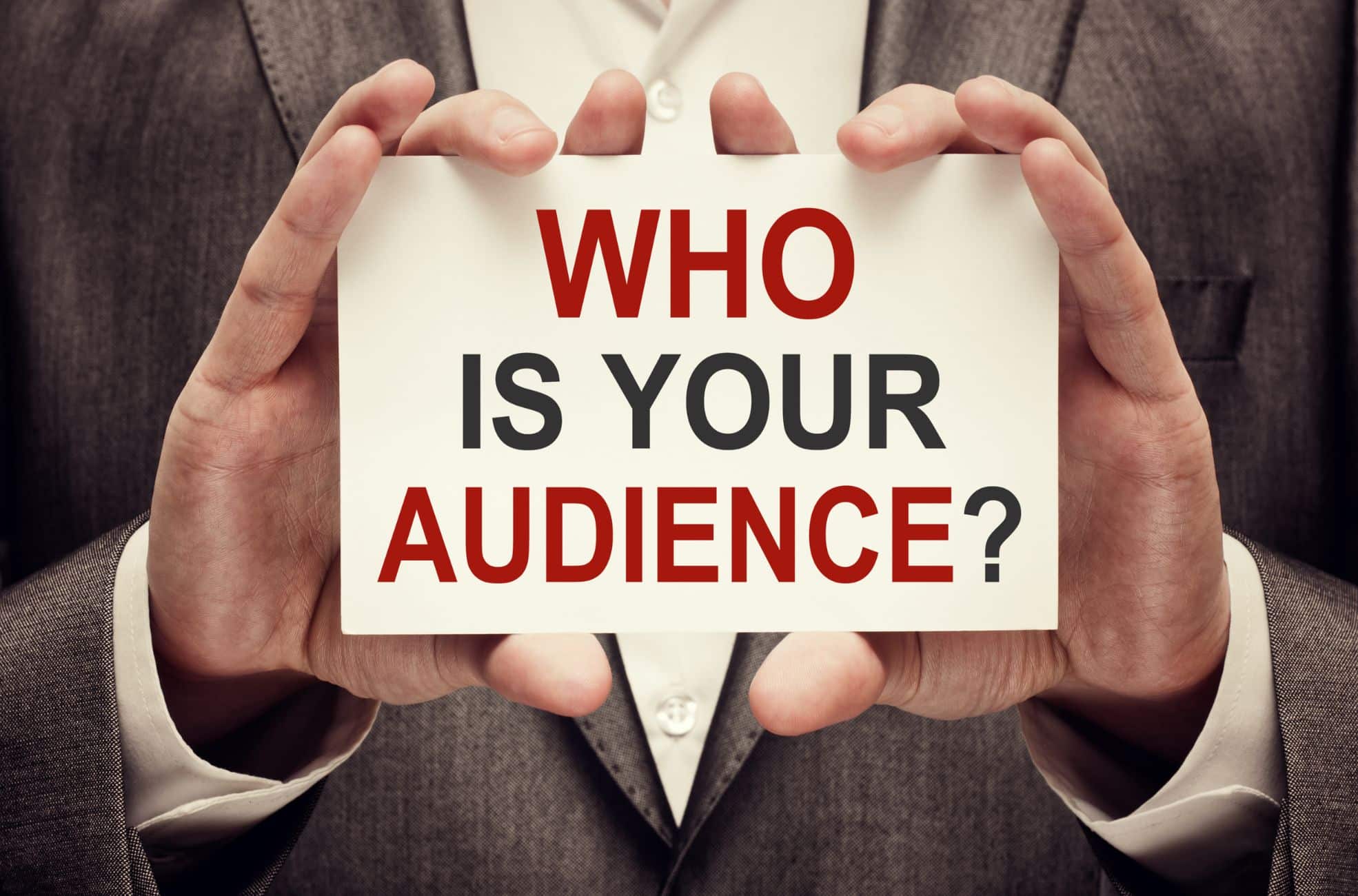 Business Man Holding Sign Saying "Who Is Your Audience?"